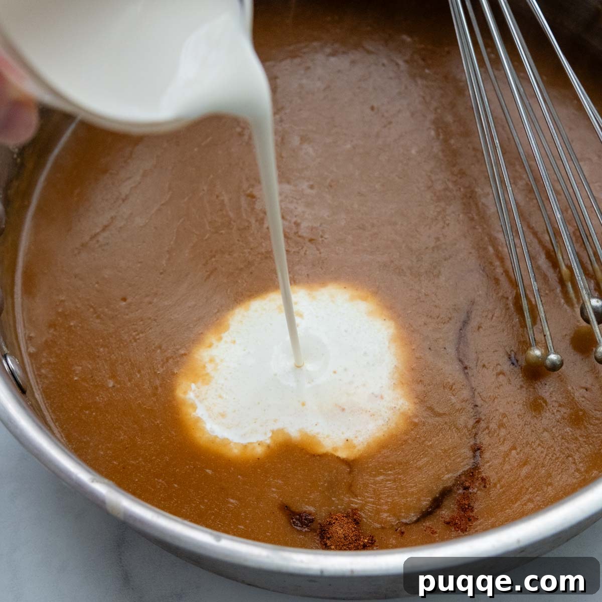 Effortless Oven Baked Gluten-Free Swedish Meatballs 7 Creamy half and half being poured into the simmering gravy mixture in a skillet.