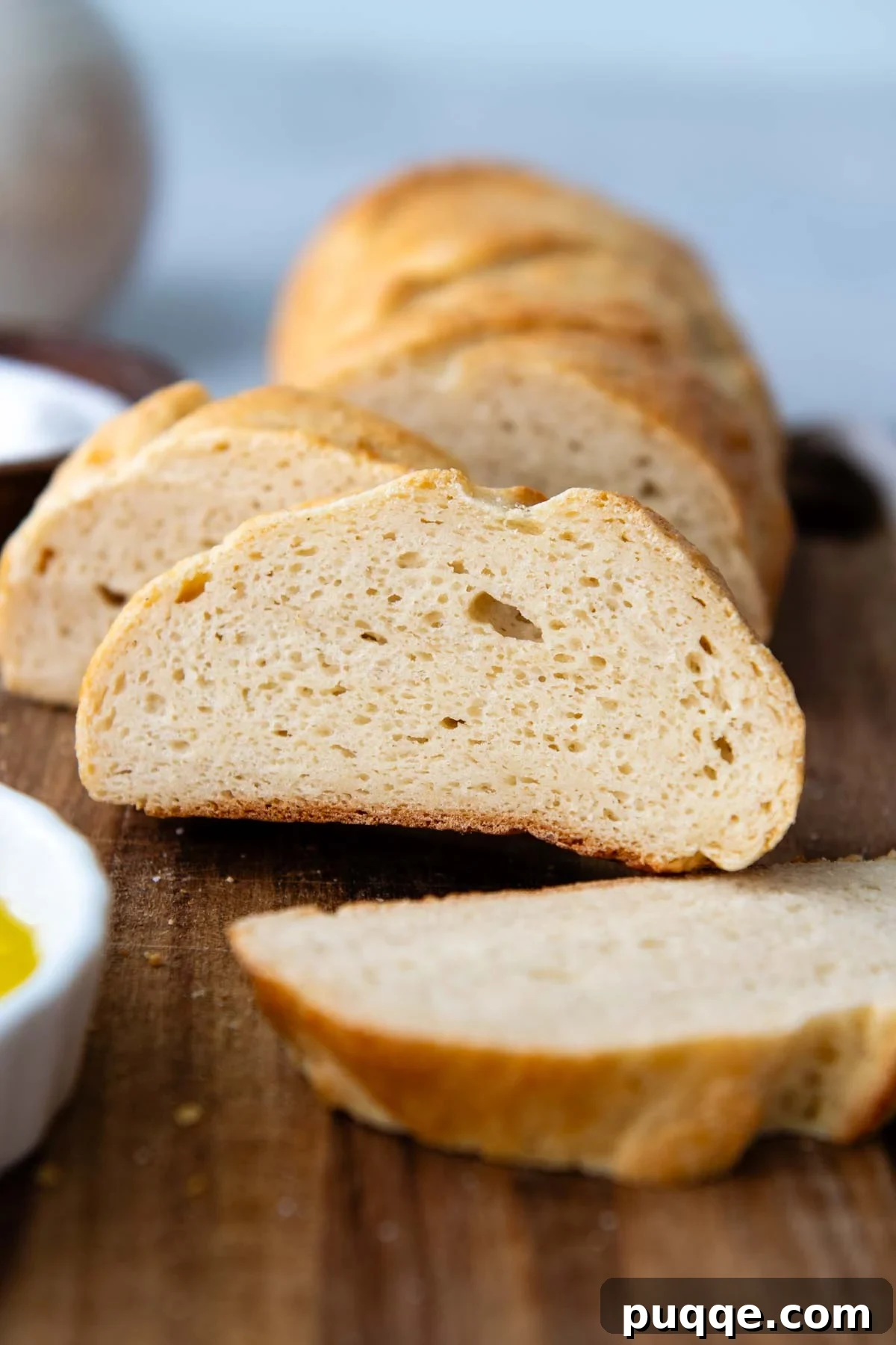 Effortless Homemade Gluten-Free Italian Bread 2 Slices of freshly baked gluten-free Italian bread on a rustic wooden cutting board, showcasing its soft, airy crumb and golden crust.