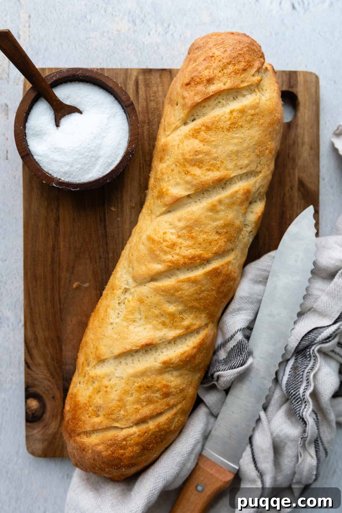 Effortless Homemade Gluten-Free Italian Bread 8 An entire golden-brown loaf of homemade gluten-free Italian bread on a wooden cutting board, with a small bowl of salt.