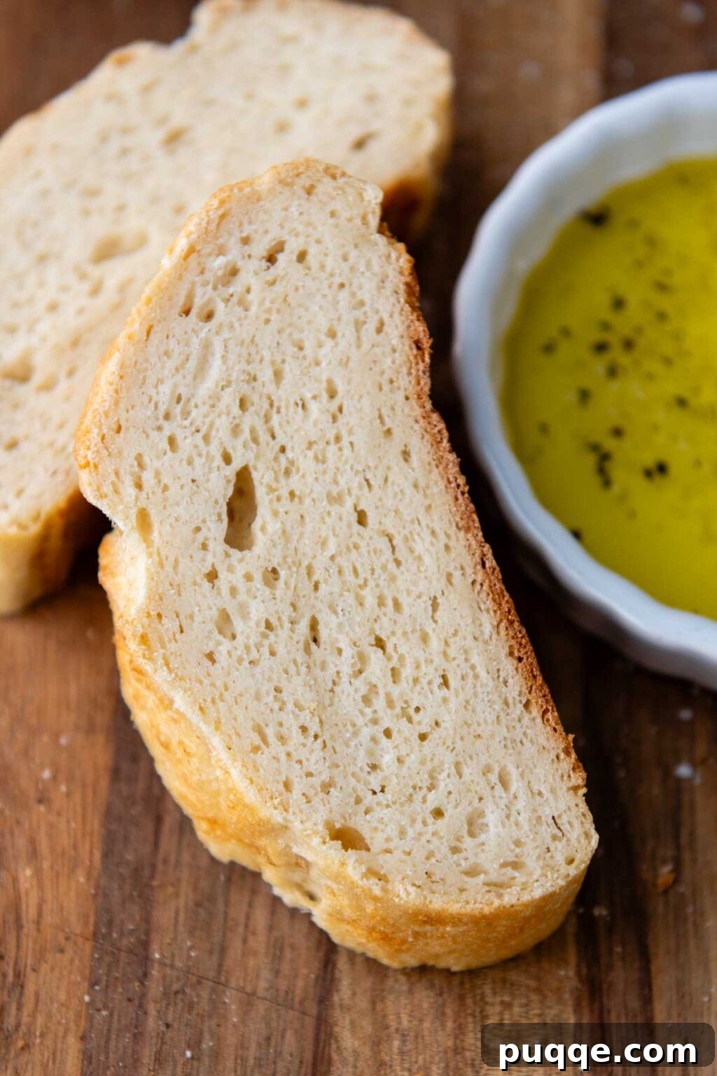 Effortless Homemade Gluten-Free Italian Bread 9 A perfectly sliced piece of gluten-free Italian bread leaning against a small bowl of olive oil, ready for dipping.