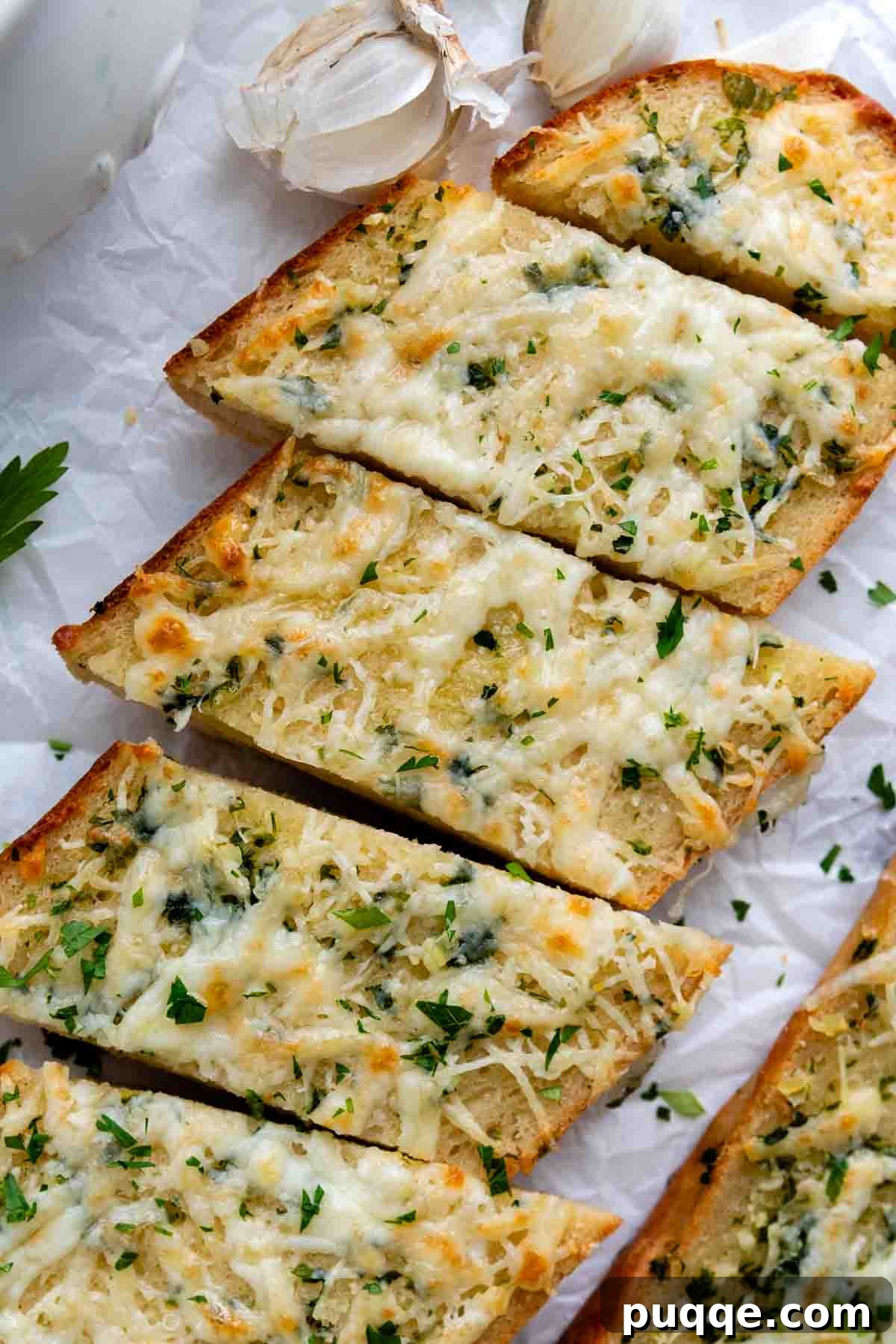 Overhead shot of freshly sliced gluten-free garlic bread with whole garlic cloves scattered next to it, highlighting the main ingredient.