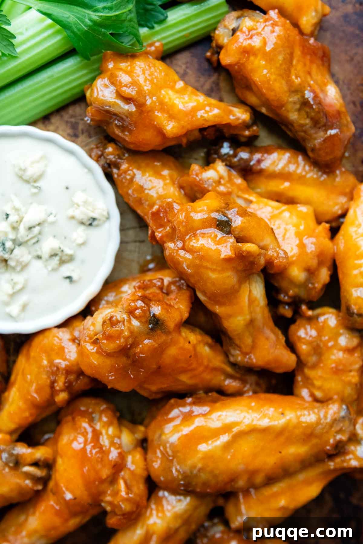 Overhead shot of freshly baked gluten-free chicken wings arranged on a wire rack on a baking sheet, with a small bowl of dipping sauce and celery in the background.