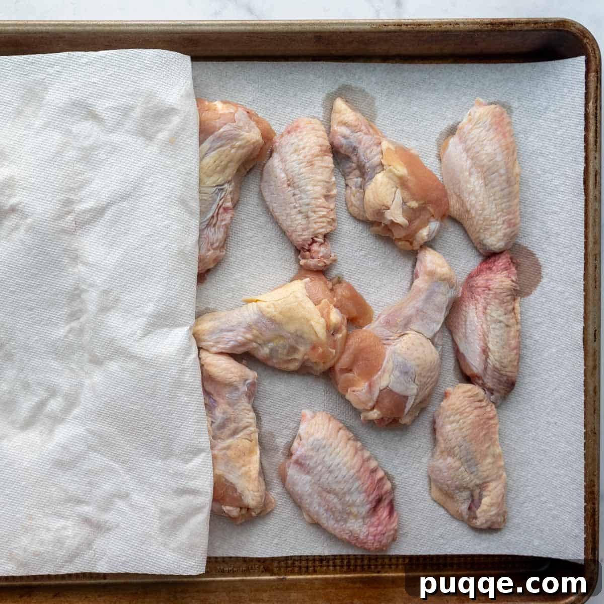 Chicken wings being patted dry with paper towels on a baking sheet, ready for seasoning.