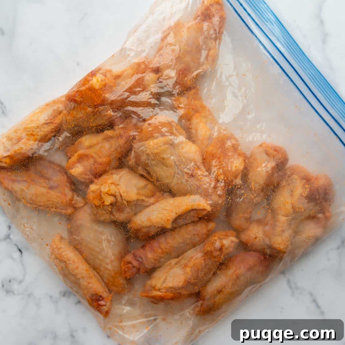Unbaked chicken wings evenly coated with a baking powder and cornstarch mixture inside a ziplock bag.