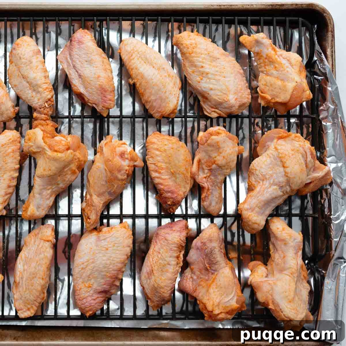 Chicken wings and drumettes perfectly arranged on a wire rack on a baking sheet, ready for the oven.
