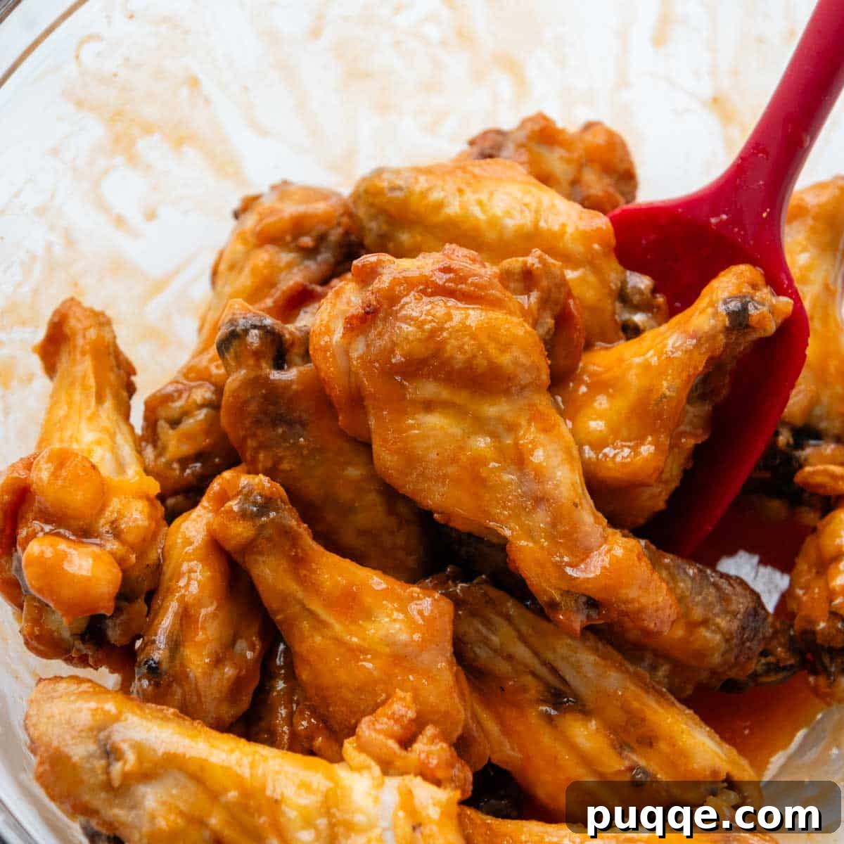 Crispy baked chicken wings being tossed in a large bowl with vibrant buffalo sauce.
