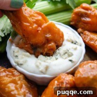 A buffalo drumette being dipped in blue cheese dressing, highlighting its crispy texture.