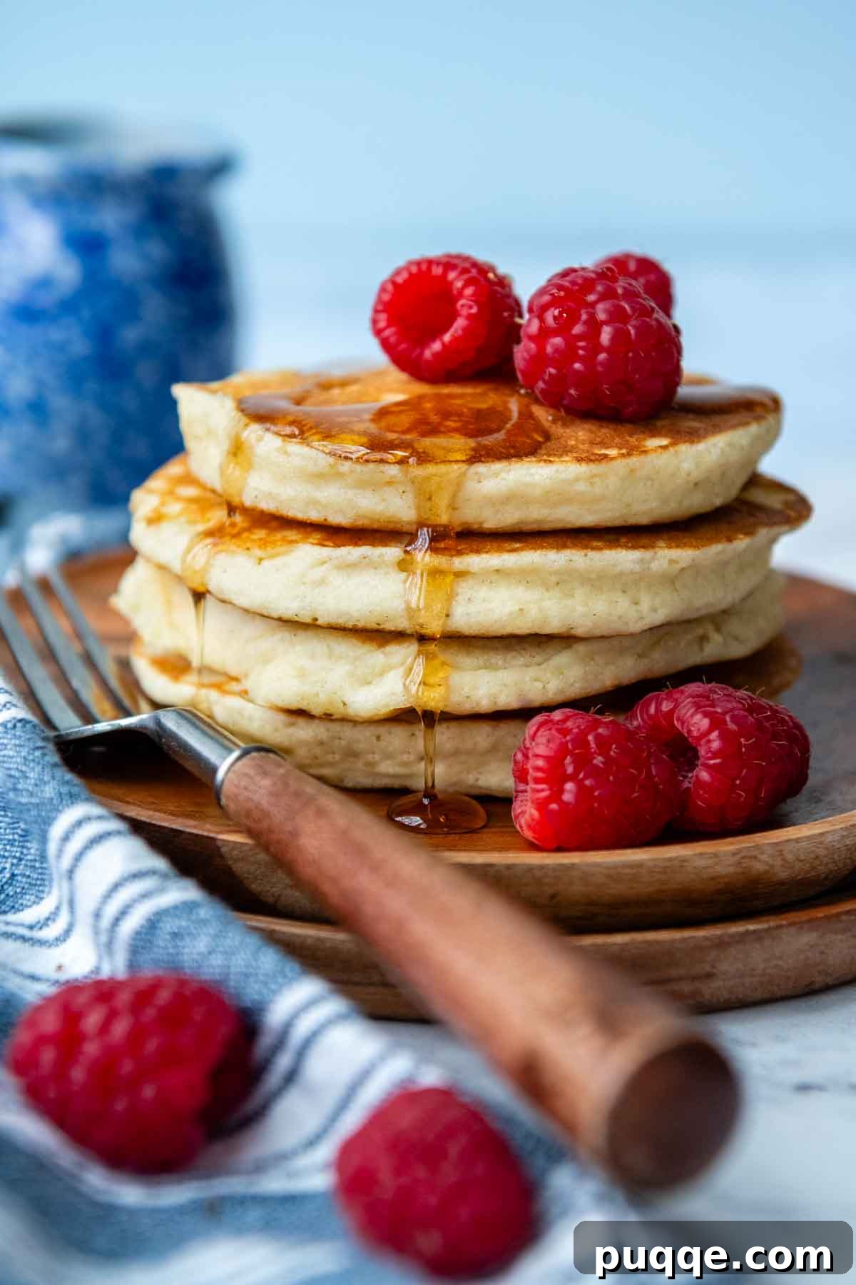A beautifully stacked plate of golden gluten-free pancakes, garnished with fresh raspberries and a drizzle of maple syrup, inviting indulgence.