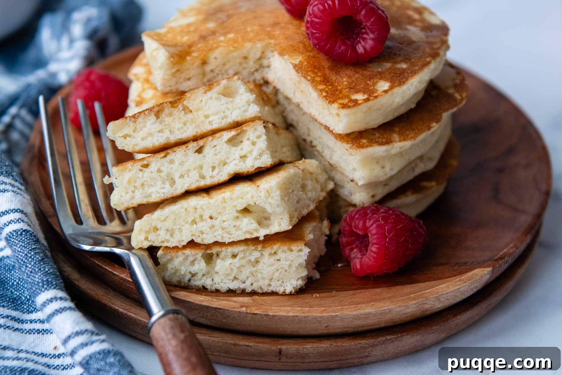 A close-up shot of a single gluten-free pancake with a bite taken out, revealing its airy, fluffy interior, placed on a rustic wooden plate.
