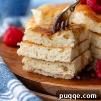 A fork stabbing into a stacked bite of fluffy gluten-free pancakes, garnished with berries.