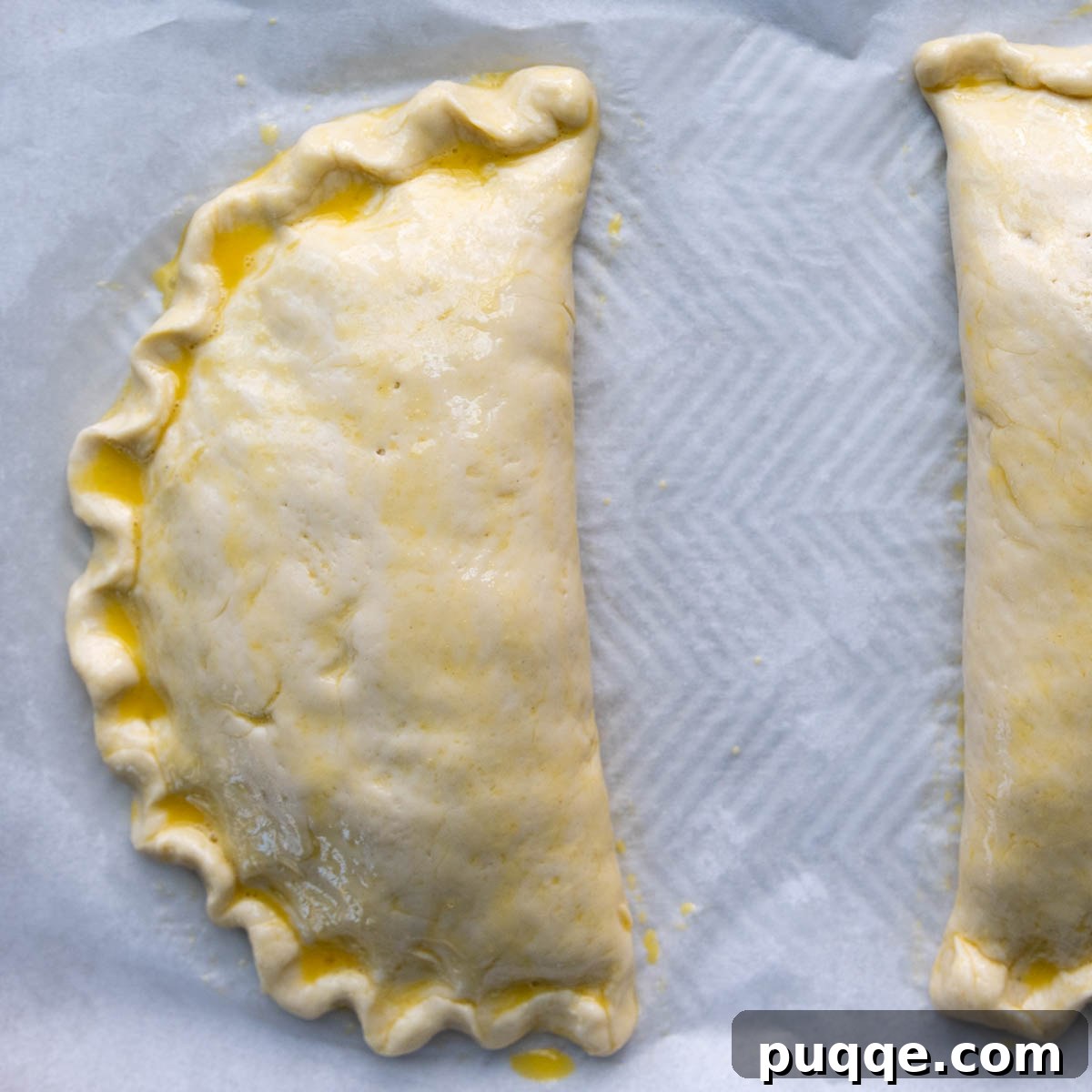 Pillowy Soft Gluten-Free Calzones 10 Unbaked gluten-free calzones on a baking sheet, glistening after being brushed with a golden egg wash.