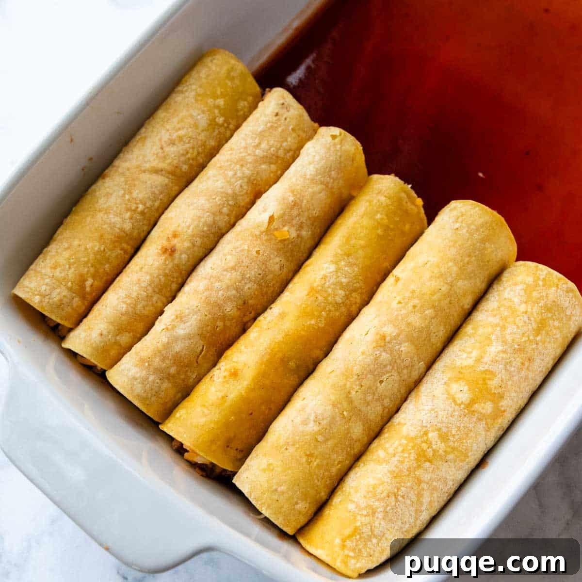Ultimate Gluten-Free Cheesy Beef and Bean Enchiladas 7 Twelve rolled enchiladas neatly arranged in two rows within a baking dish.