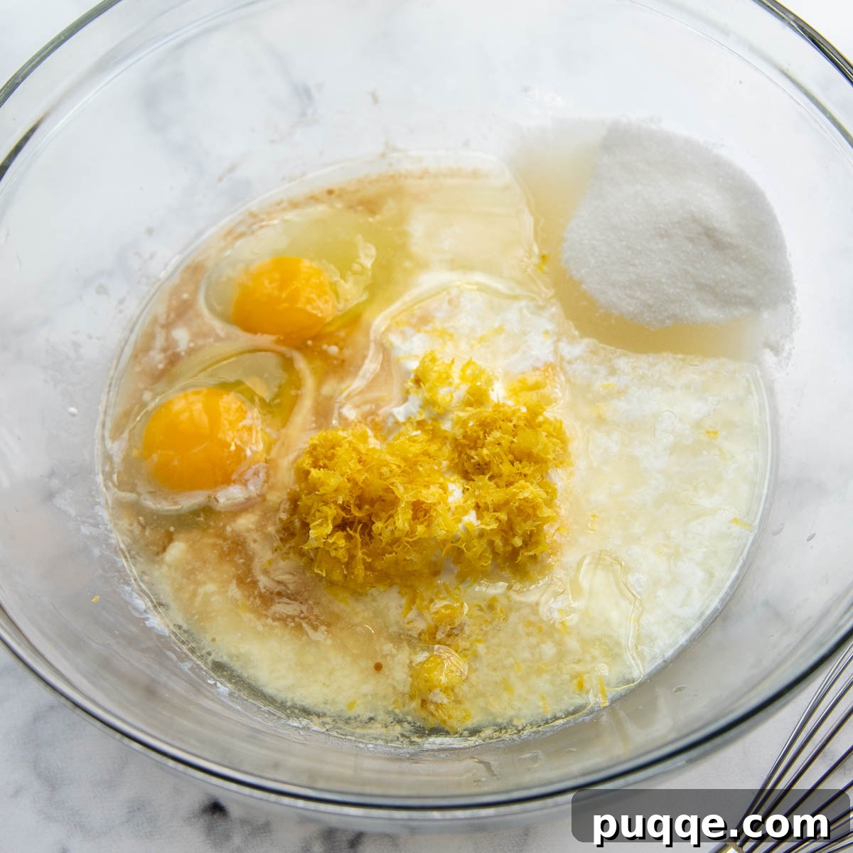 A glass bowl filled with the whisked wet ingredients for lemon poppy seed muffins, showing the vibrant yellow hue of lemon.