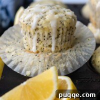 a lemon muffin with poppy seeds on an opened paper liner with glaze on top.