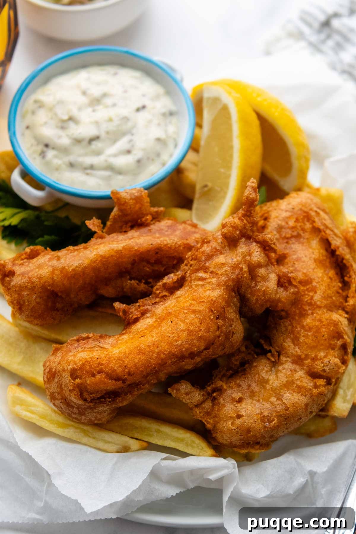 a serving of fish and chips with tartar sauce and lemons.