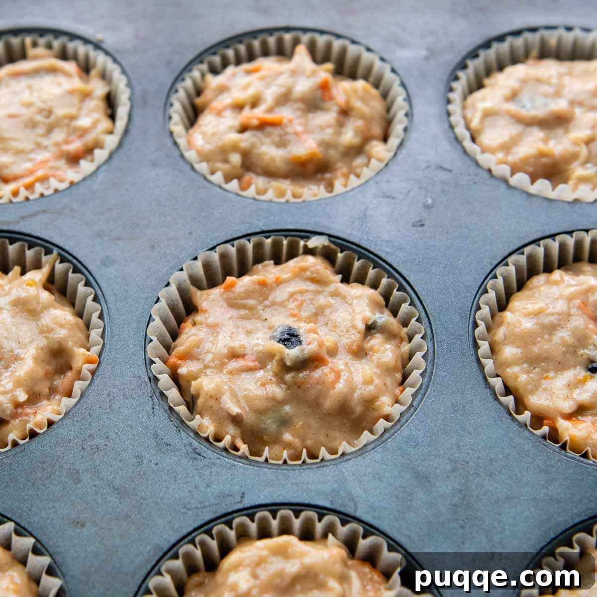 A muffin tin with liners almost completely filled with unbaked muffin batter, ready for the oven.