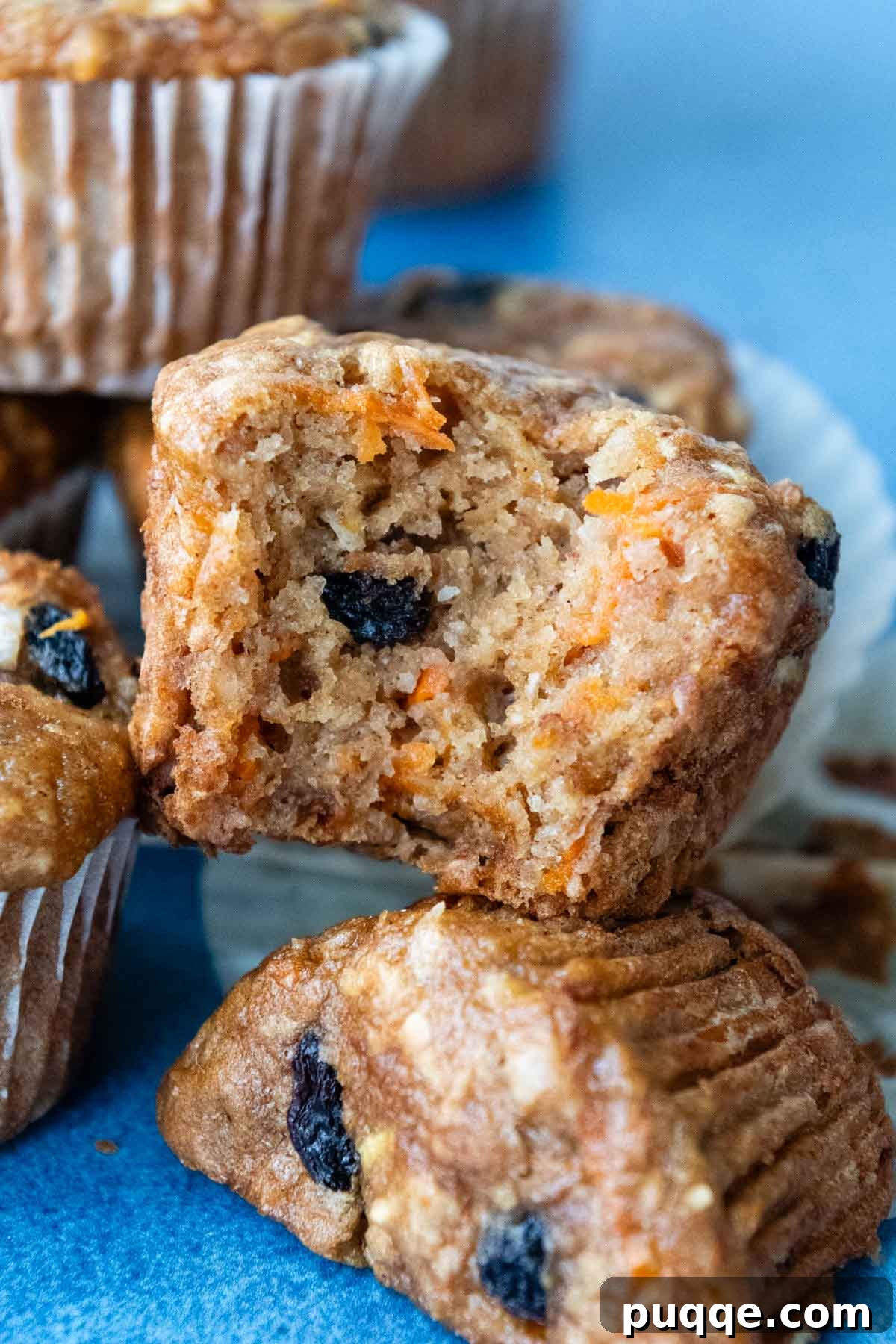 A close-up shot of a gluten-free morning glory muffin with a bite taken out, stacked on top of other muffins, showcasing its moist interior.