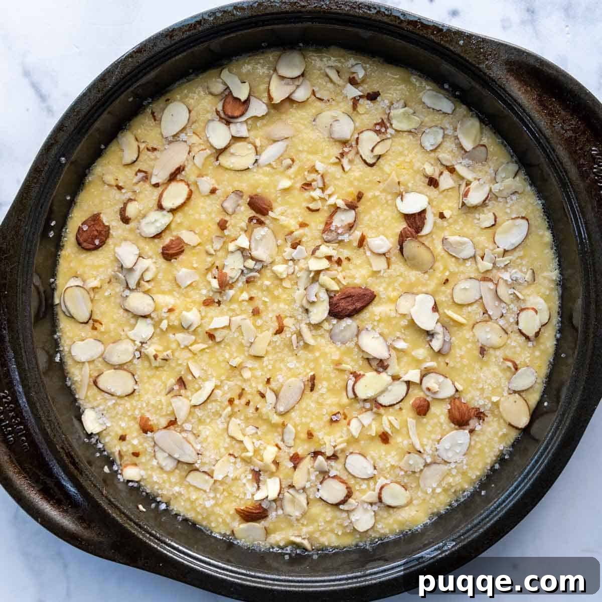 Unbaked almond flour lemon cake batter in a pan, topped with a generous sprinkle of sliced almonds and turbinado sugar, ready for the oven.
