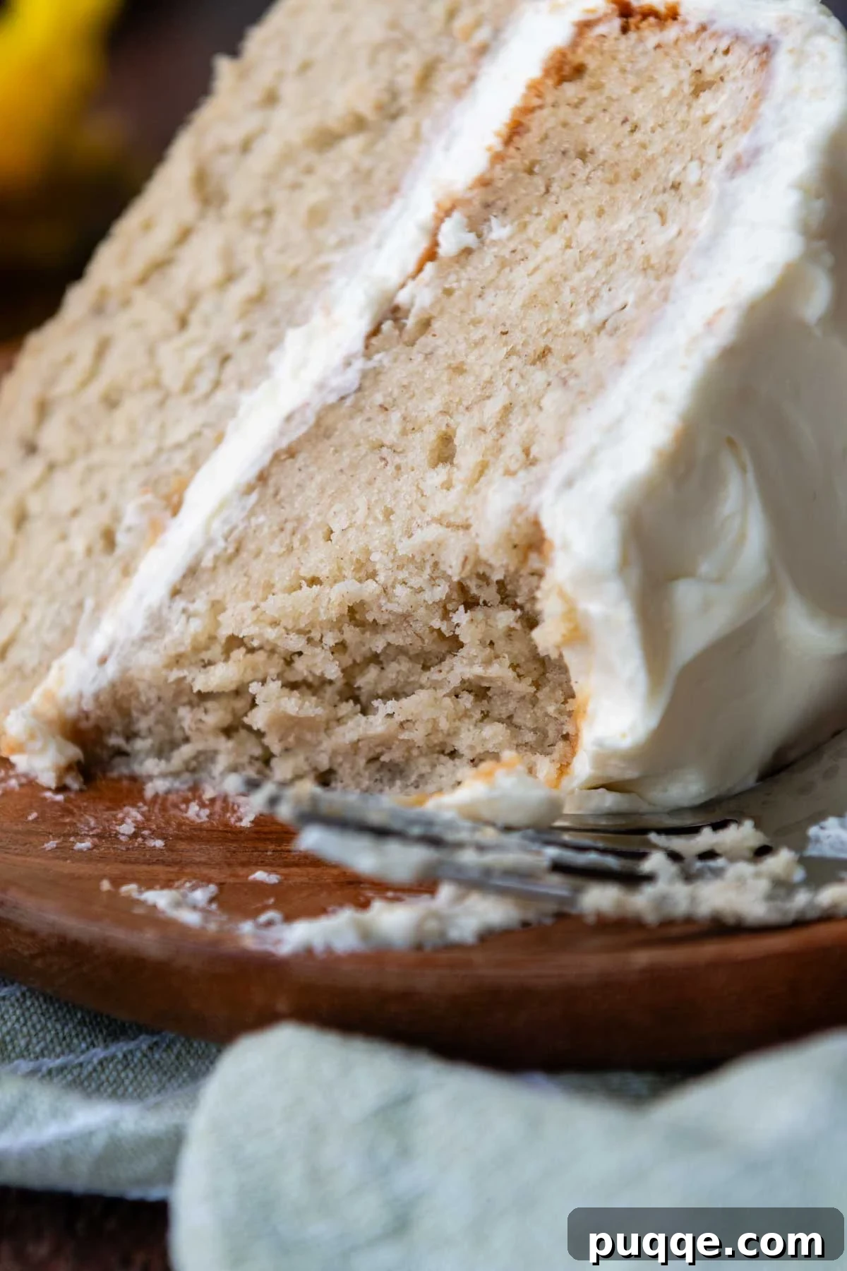 Cloud-Like Gluten-Free Banana Cake 2 A perfectly sliced piece of fluffy gluten-free banana cake with light whipped cream cheese frosting and a bite taken out, showing its moist and airy crumb.