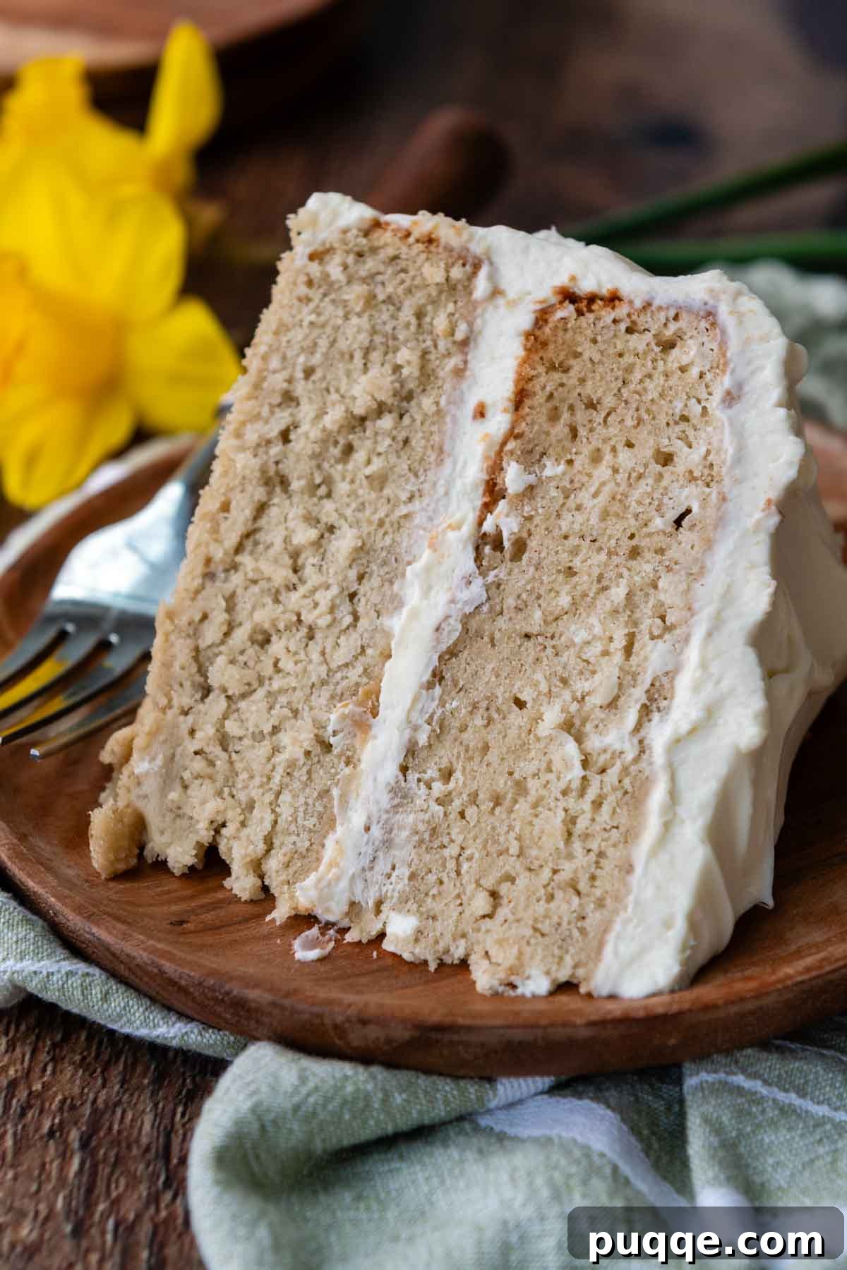 Cloud-Like Gluten-Free Banana Cake 3 A moist slice of gluten-free banana cake topped with cream cheese frosting, resting on a rustic wooden plate.