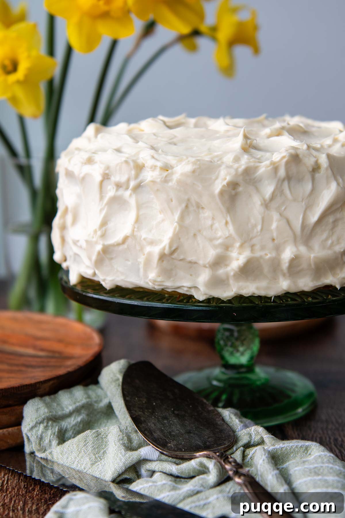 Cloud-Like Gluten-Free Banana Cake 9 A beautifully frosted whole gluten-free banana cake on a vibrant green platter, with soft background flowers.