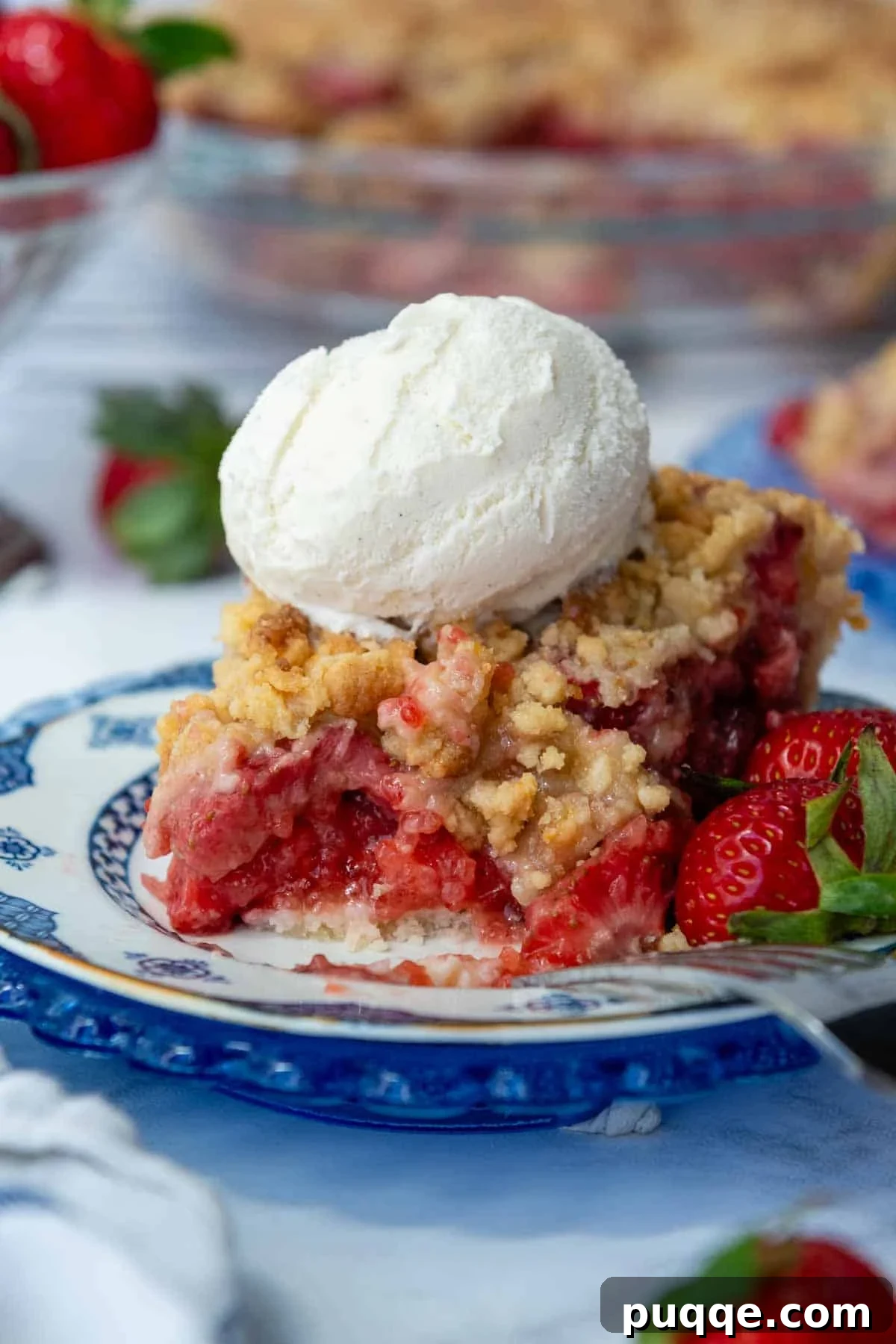 A glorious slice of gluten-free strawberry pie, topped with a scoop of vanilla ice cream and a small bite taken out, revealing the vibrant strawberry filling and crumbly streusel.