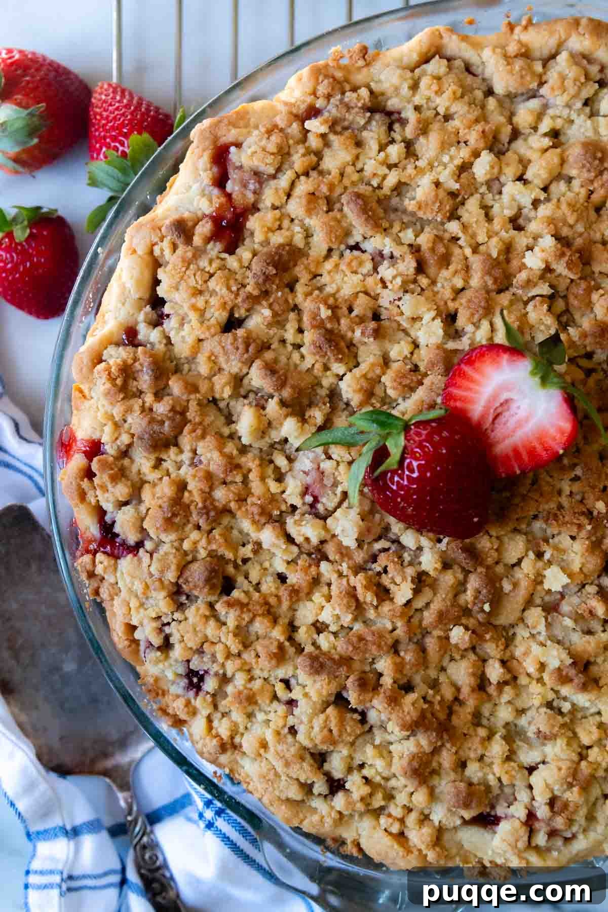 An overhead shot of an unsliced, freshly baked gluten-free strawberry pie resting on a cooling rack, showcasing its golden streusel topping and bubbling filling.
