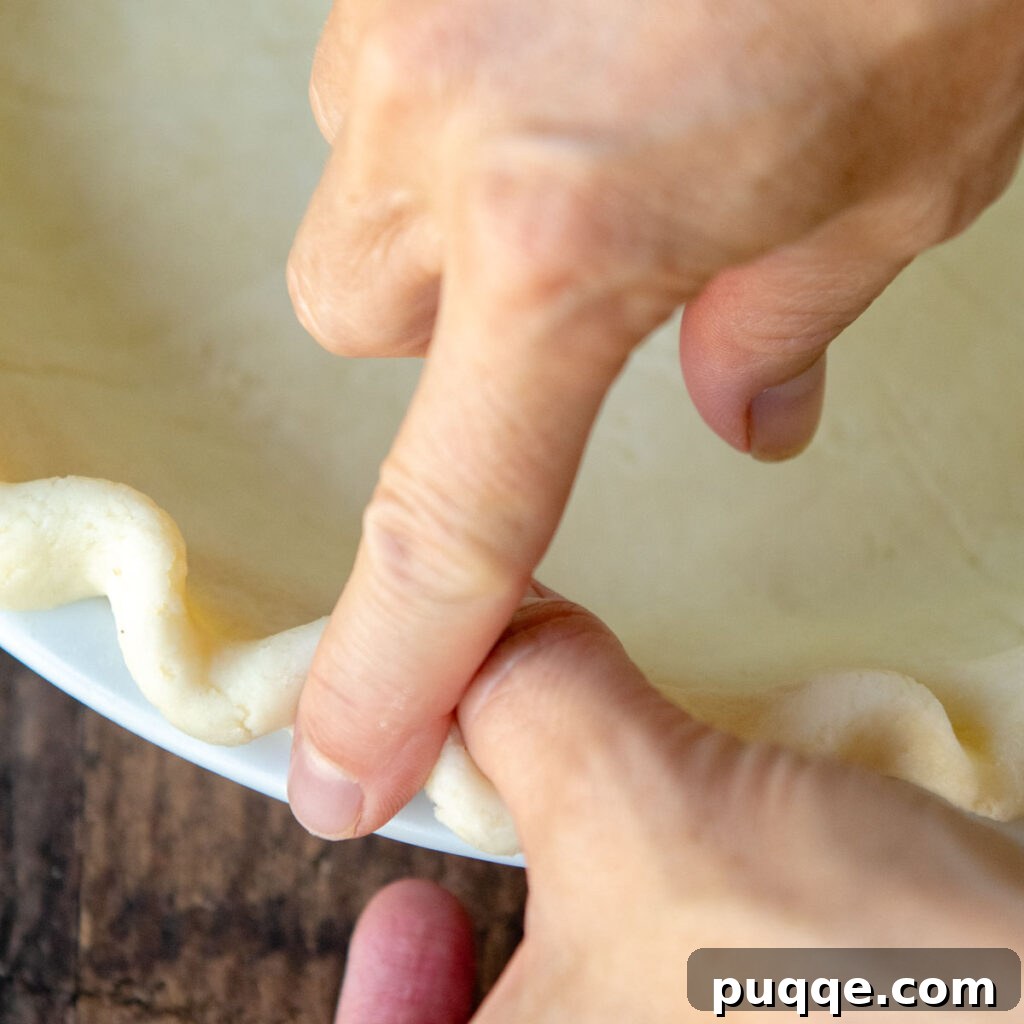Fingers expertly crimping the edges of a gluten-free pie crust into a decorative flute pattern, ready for baking.