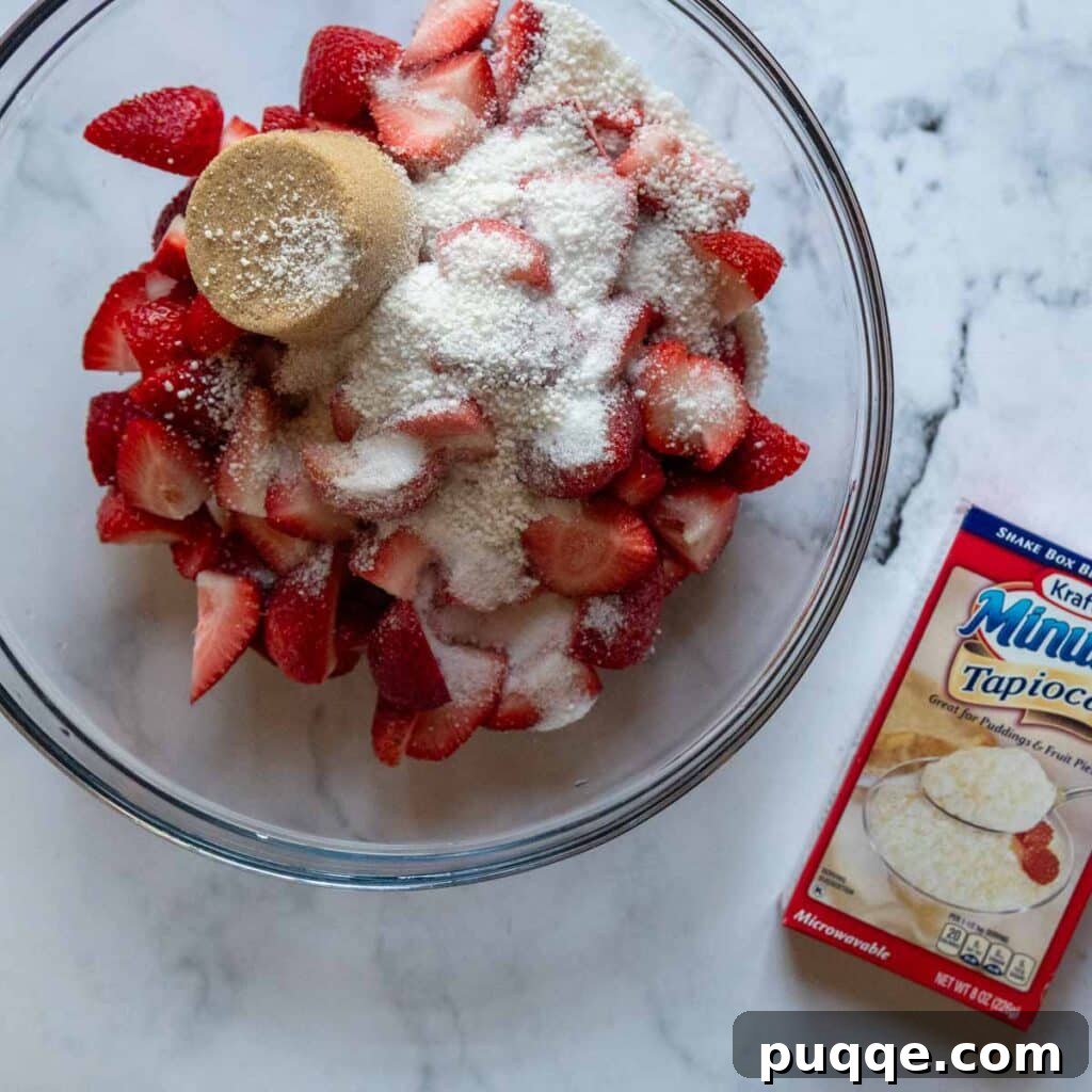 A large bowl containing the ingredients for the strawberry pie filling, with a box of instant tapioca visible beside it, highlighting the key thickener.