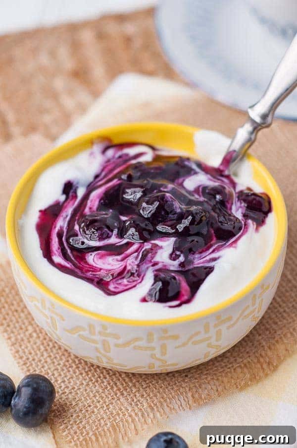 Homemade 10-Minute Maple Blueberry Syrup 6 Vibrant blueberry syrup swirled into a small bowl of creamy yogurt, showcasing its beautiful color.