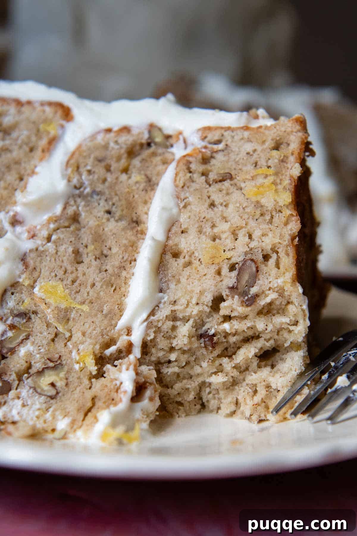 Tropical & Tender Gluten-Free Hummingbird Cake 2 A beautifully decorated slice of gluten-free hummingbird cake on a white plate, with a bite taken out, showcasing its moist layers and creamy frosting.