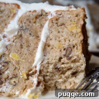 A close-up slice of gluten-free hummingbird cake on a white plate with a fork, showing its moist texture and frosting.