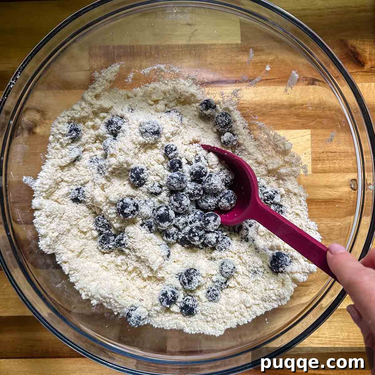 Fresh blueberries being gently folded into the sandy flour and butter mixture.