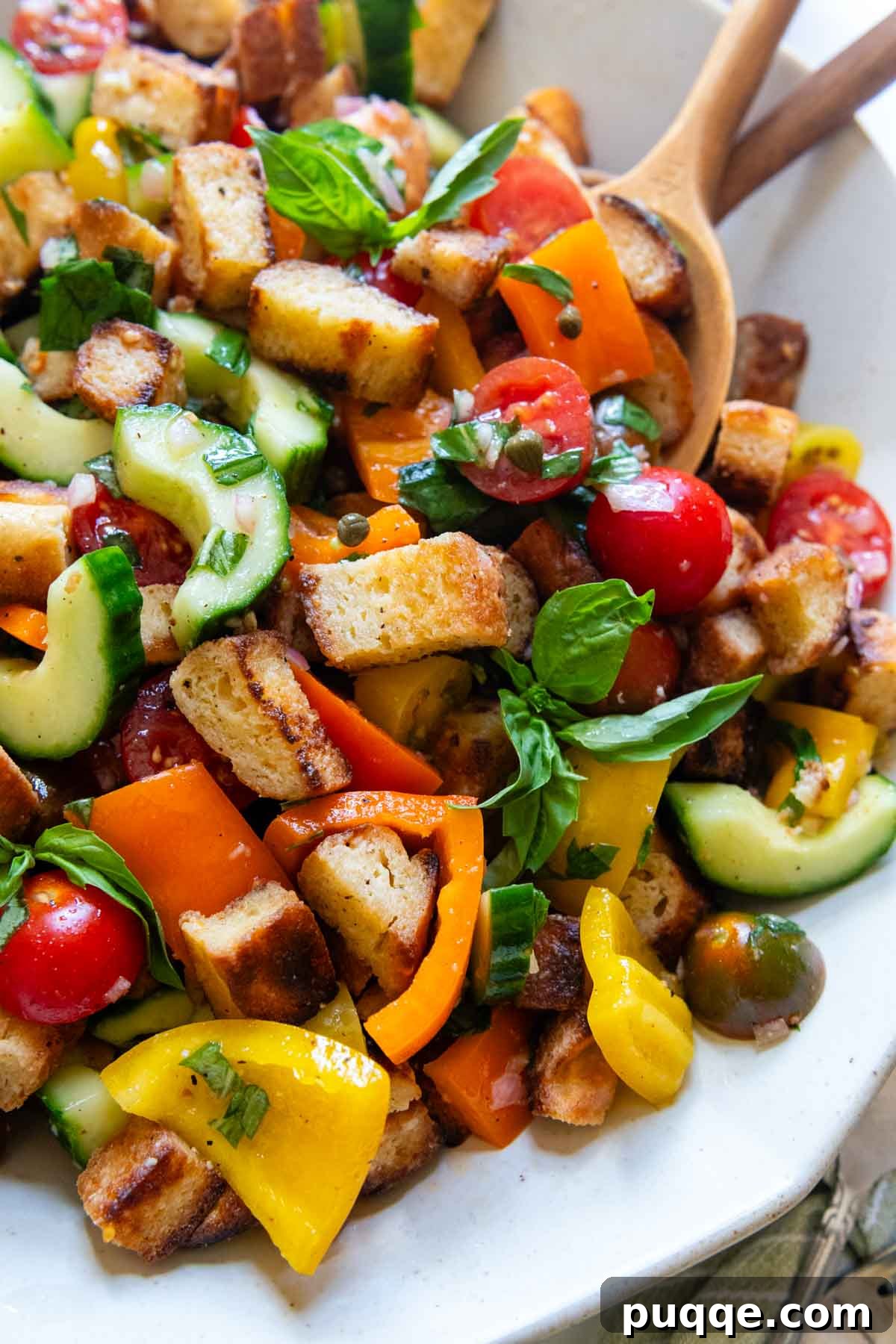 A close-up view of a vibrant gluten-free Panzanella salad arranged on a pristine white serving platter, with serving utensils elegantly placed alongside.
