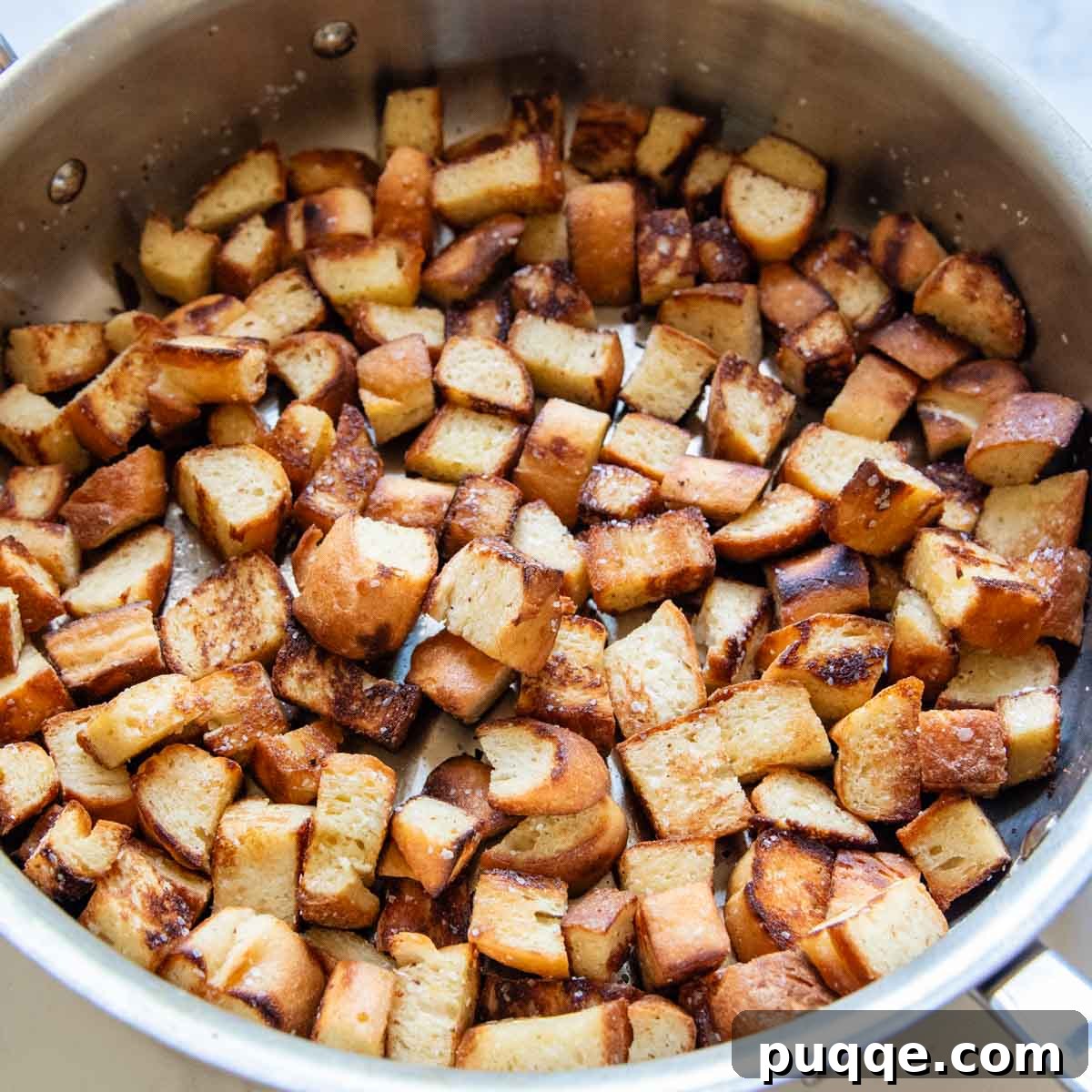 Gluten-free bread cubes being toasted to a golden crisp in a hot skillet, ready for the Panzanella salad.