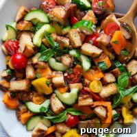 Overhead shot of gluten-free Panzanella salad in a white serving bowl, garnished with fresh basil.