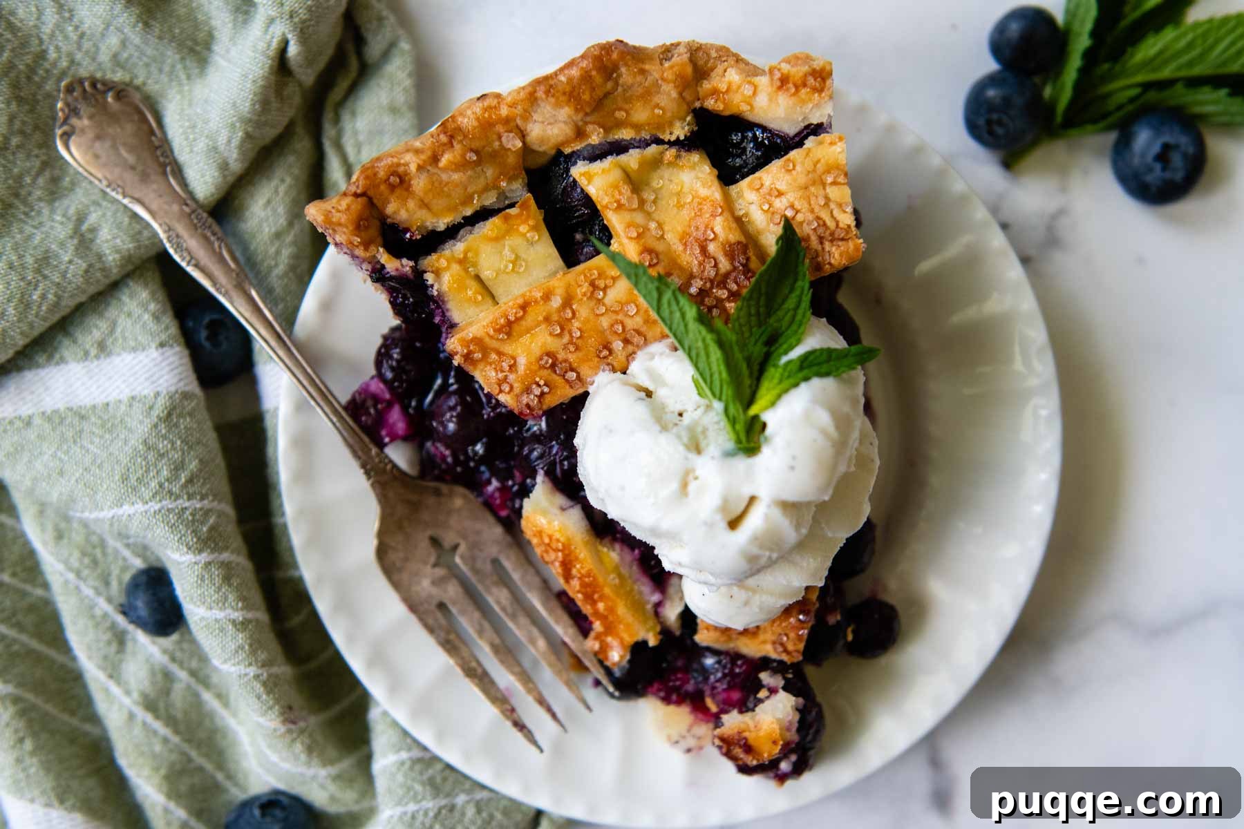 An inviting overhead shot of a freshly baked gluten-free blueberry lattice pie, artfully topped with a dollop of vanilla ice cream, promising a delightful dessert experience.
