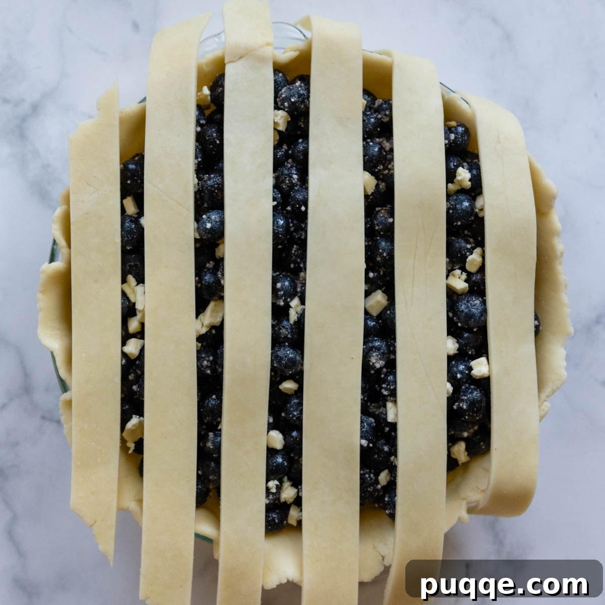 The initial stage of weaving a lattice pie crust, with vertical strips laid out over the blueberry filling.