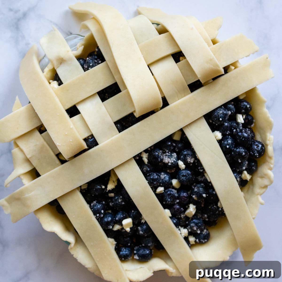 A close-up demonstration of how to weave a lattice pie crust over a juicy blueberry filling, showing the intricate pattern.