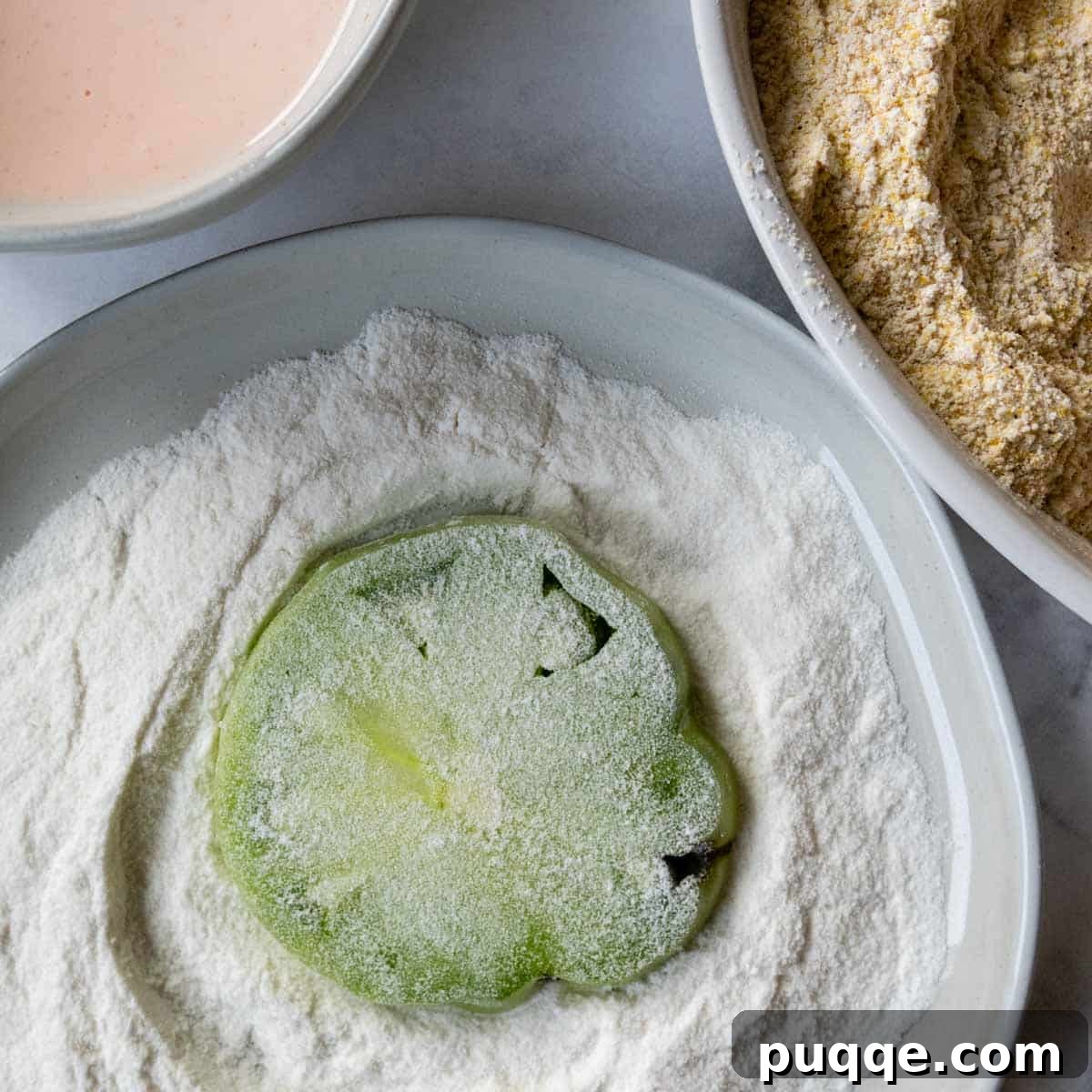 A sliced green tomato being dredged in white rice flour.