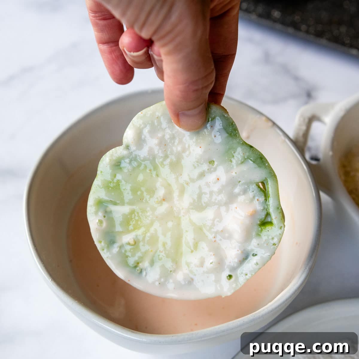 A green tomato slice emerging from the seasoned buttermilk mixture.