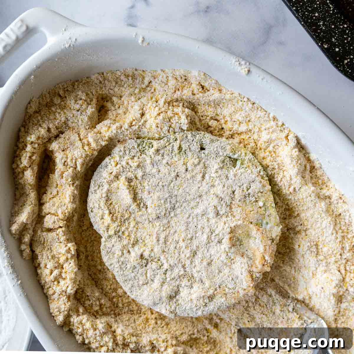 A sliced green tomato being pressed into the crispy cornmeal breading.