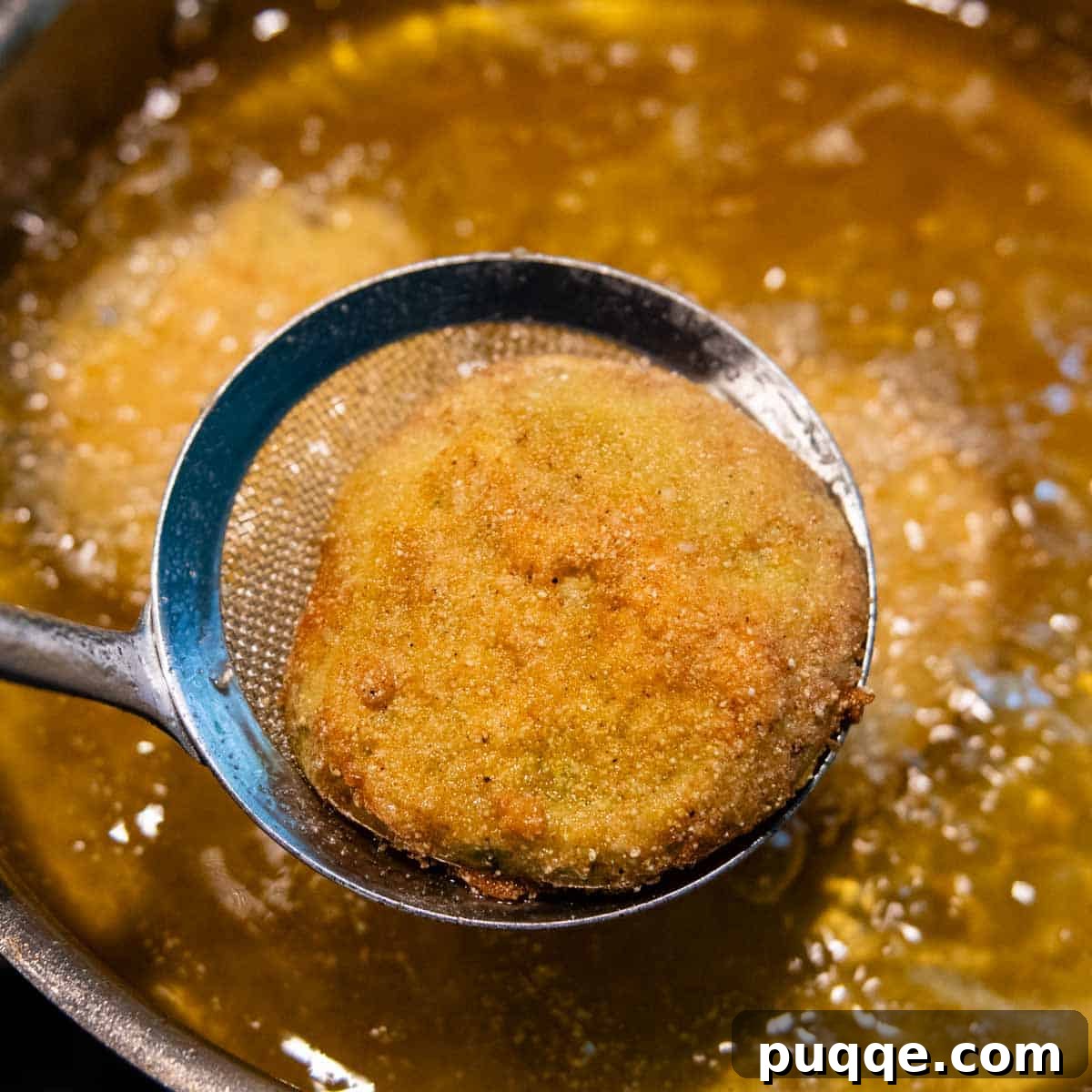 A skimmer spoon carefully lifting a perfectly fried green tomato out of the hot oil.