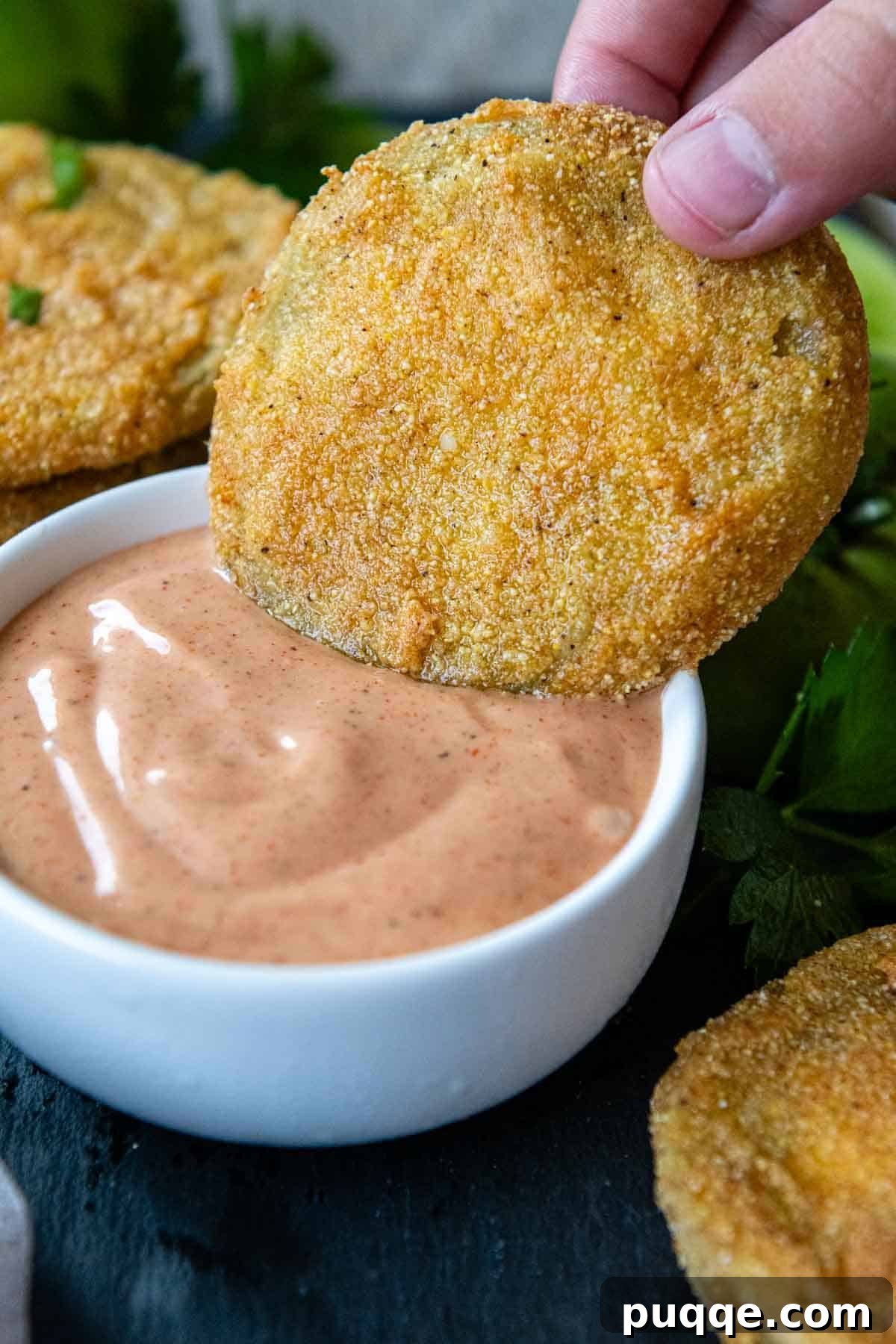 A crispy fried green tomato being generously dipped into a creamy, zesty comeback sauce.