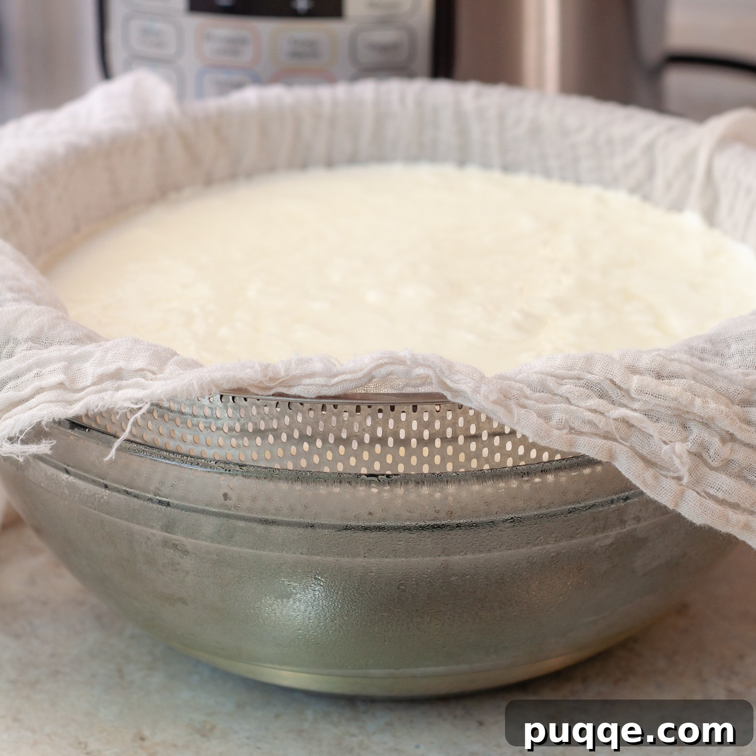 Yogurt being poured into a cheesecloth-lined strainer over a bowl to separate whey.