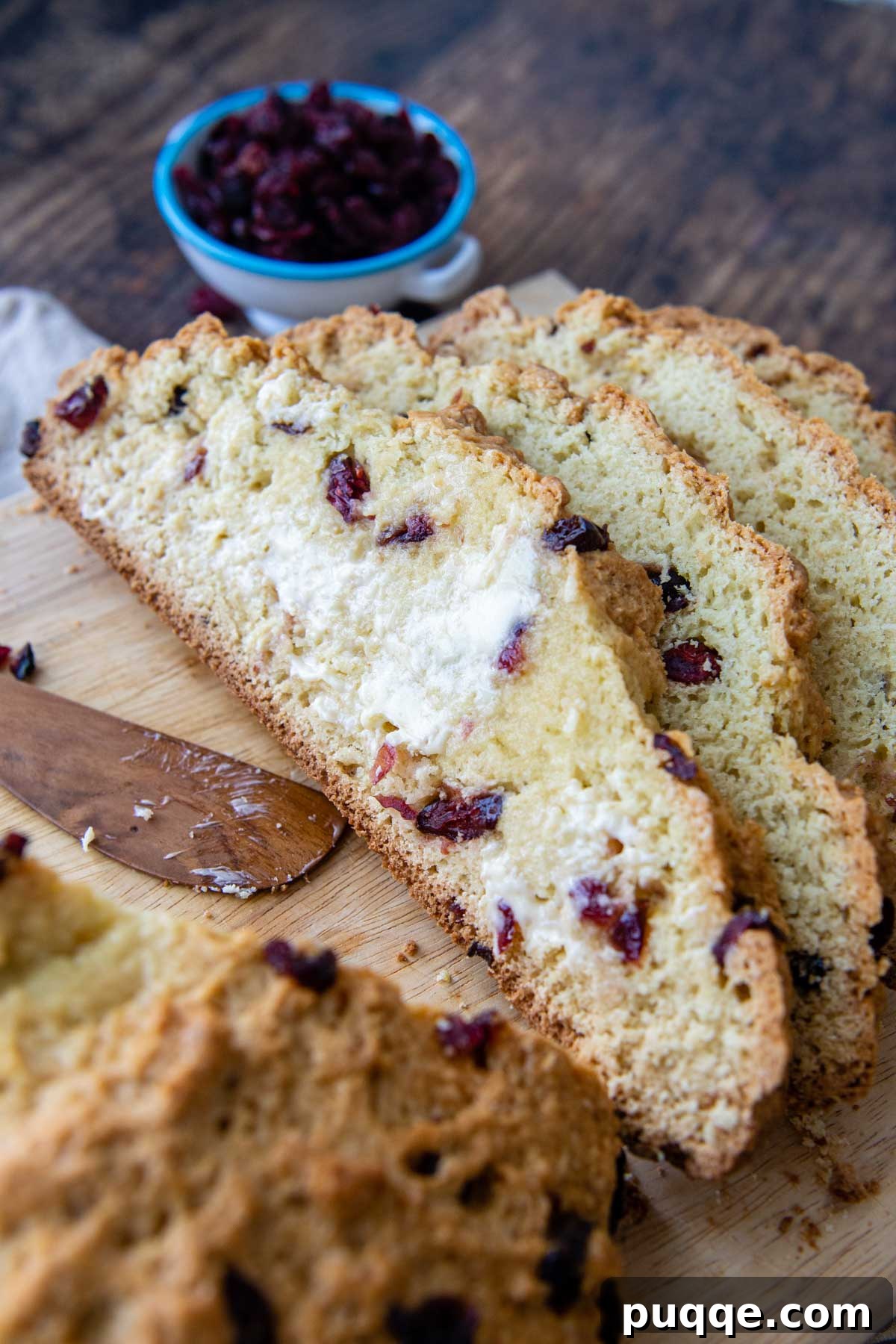 Melt-in-Your-Mouth Sweet Irish Soda Bread 7 Slices of sweet Irish soda bread with dried cranberries visible, arranged on a wooden board with melting butter nearby.