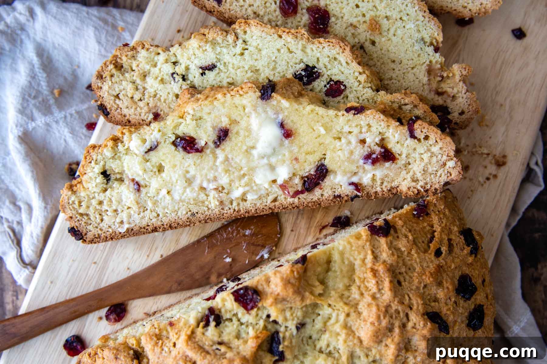 Melt-in-Your-Mouth Sweet Irish Soda Bread 8 Several slices of sweet Irish soda bread, revealing the moist interior dotted with cranberries, arranged on a wooden cutting board.