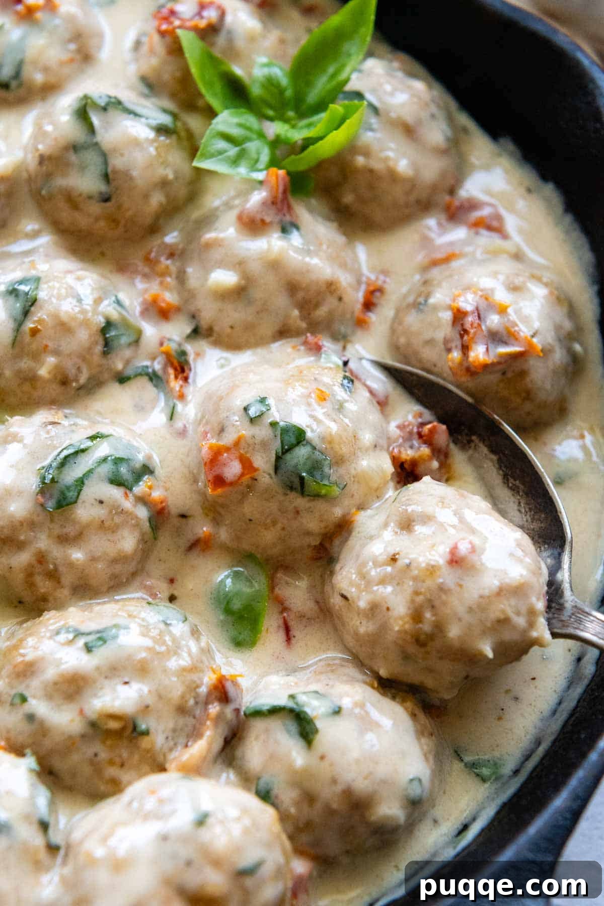 Crave-Worthy Gluten-Free Chicken Meatballs 3 A single baked chicken meatball being lifted out of a creamy sun-dried tomato sauce with a slotted spoon, ready to be served.