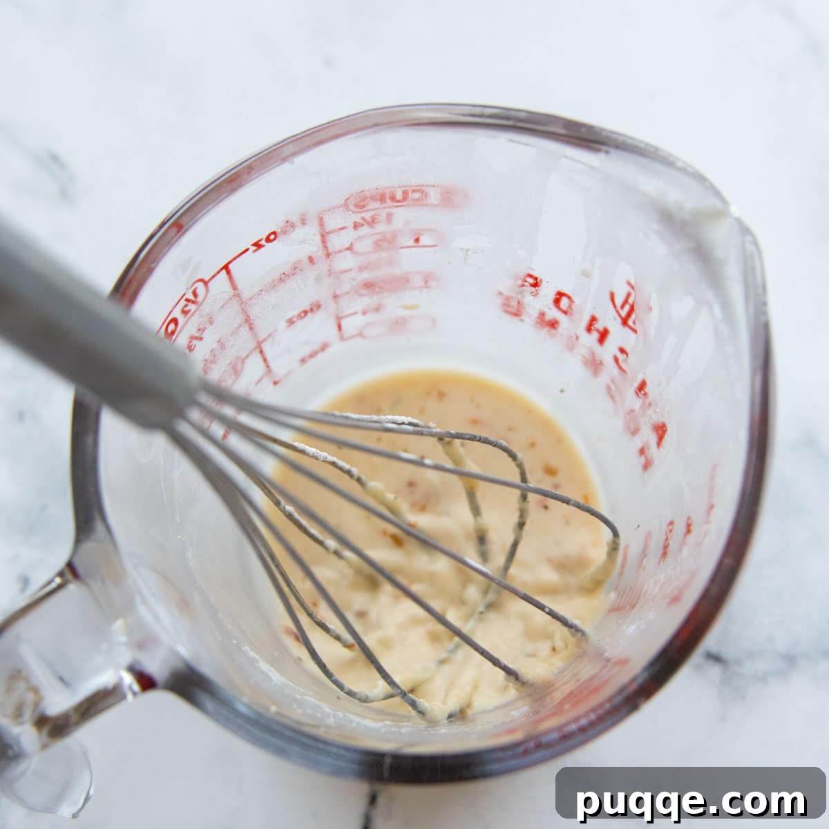 Crave-Worthy Gluten-Free Chicken Meatballs 6 A whisk vigorously mixing a cornstarch slurry into a liquid measuring cup, a crucial step for thickening the creamy sauce.