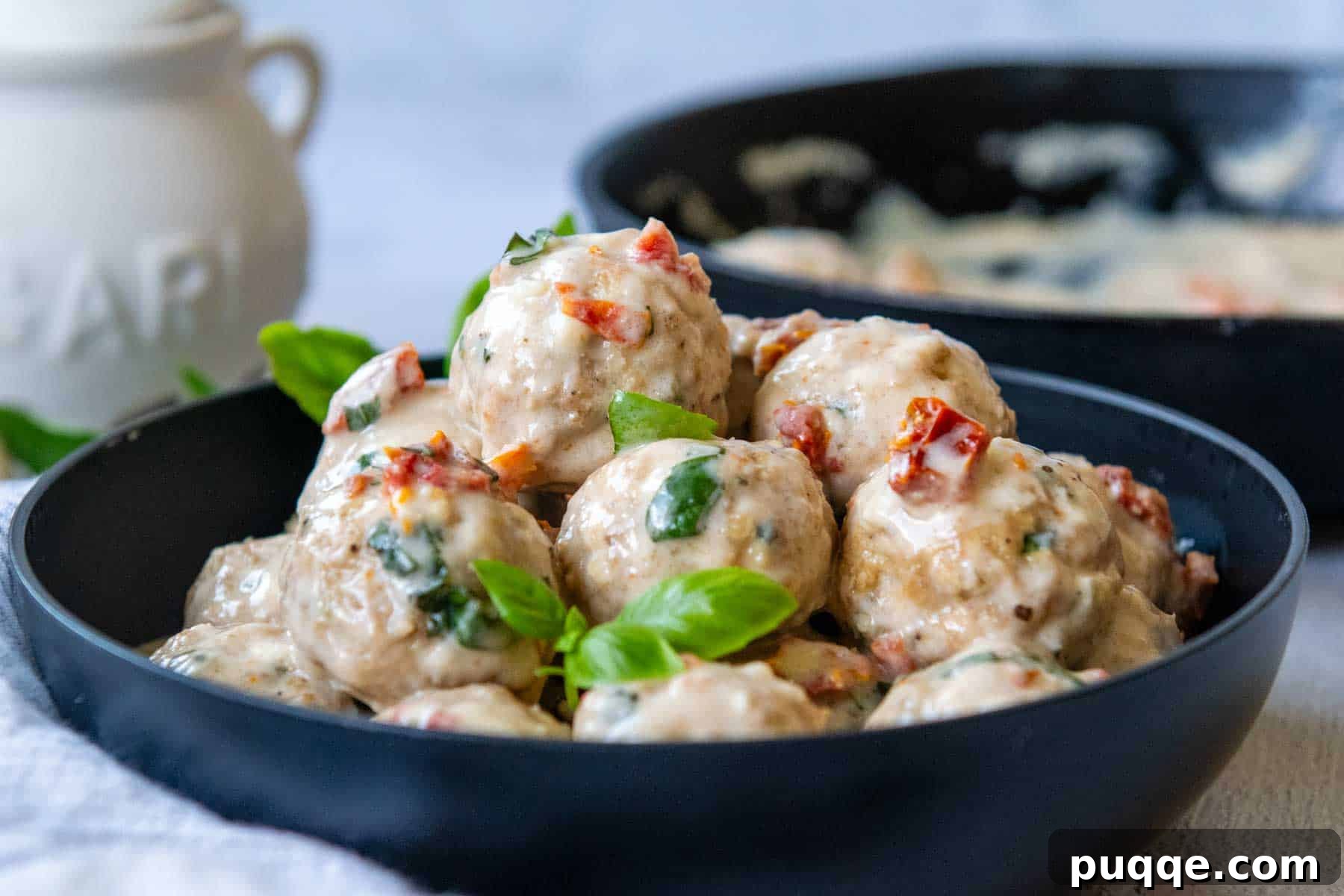 Crave-Worthy Gluten-Free Chicken Meatballs 8 A shallow black bowl brimming with delicious gluten-free chicken meatballs generously coated in creamy sun-dried tomato sauce and garnished with fresh basil leaves.